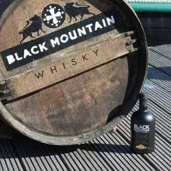 Whisky Notes Fumées-BLACK MOUNTAIN-bouteille posée sur une terrasse à coté d'une barique de whisky Black Mountain